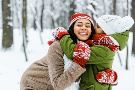 child kissing mother's cheek in the snow