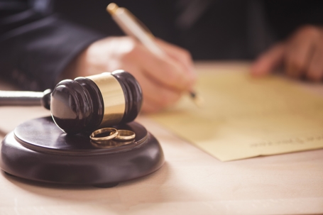 person signing divorce papers with wedding rings in the foreground