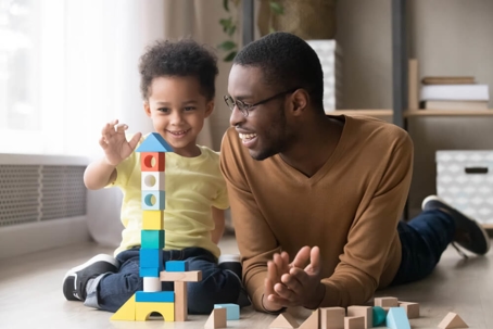 Young boy playing blocks on floor next to an older man.