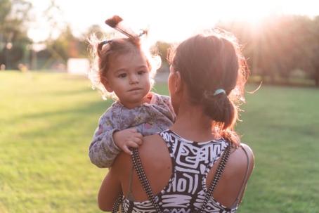 Mom holding child outdoors in urban park in golden hour.