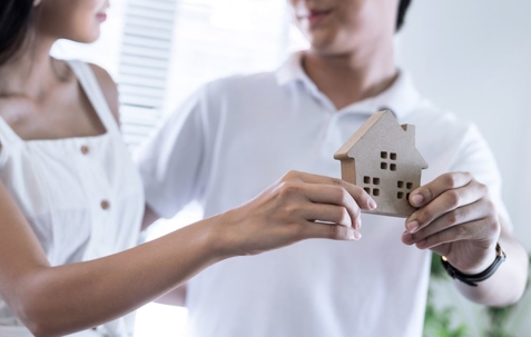 Man and woman standing and holding wooden house figure.