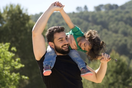 Father playing with his daughter sitting on his shoulders outside.