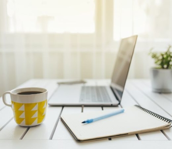 Laptop, notepad, and coffee on a desk.